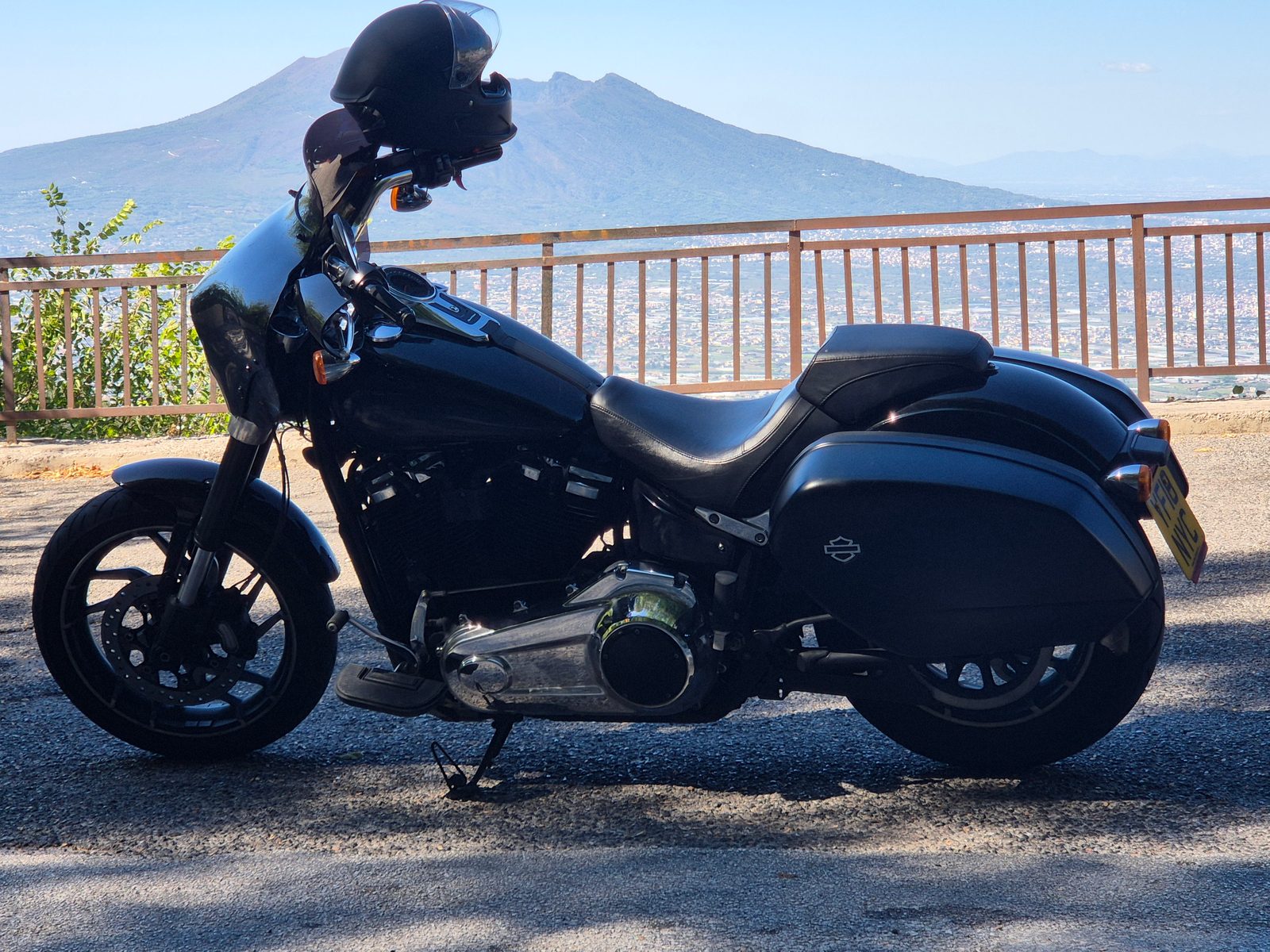 A black Harley-Davidson motorcycle parked by a railing with Mount Vesuvius and a town in the distance.