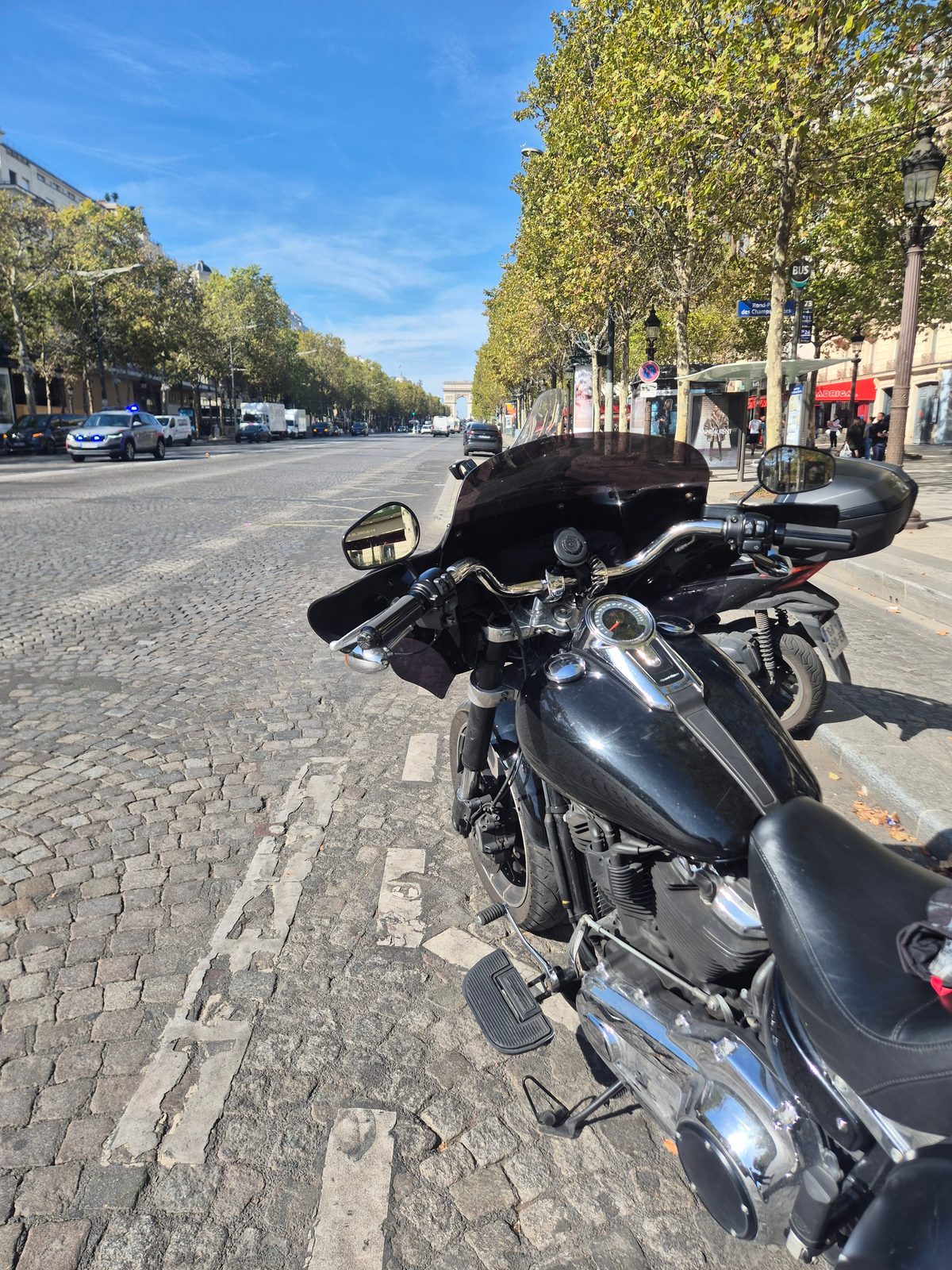 A black Harley-Davidson parked on a cobbled Paris street with the Arc de Triomphe in the distance.