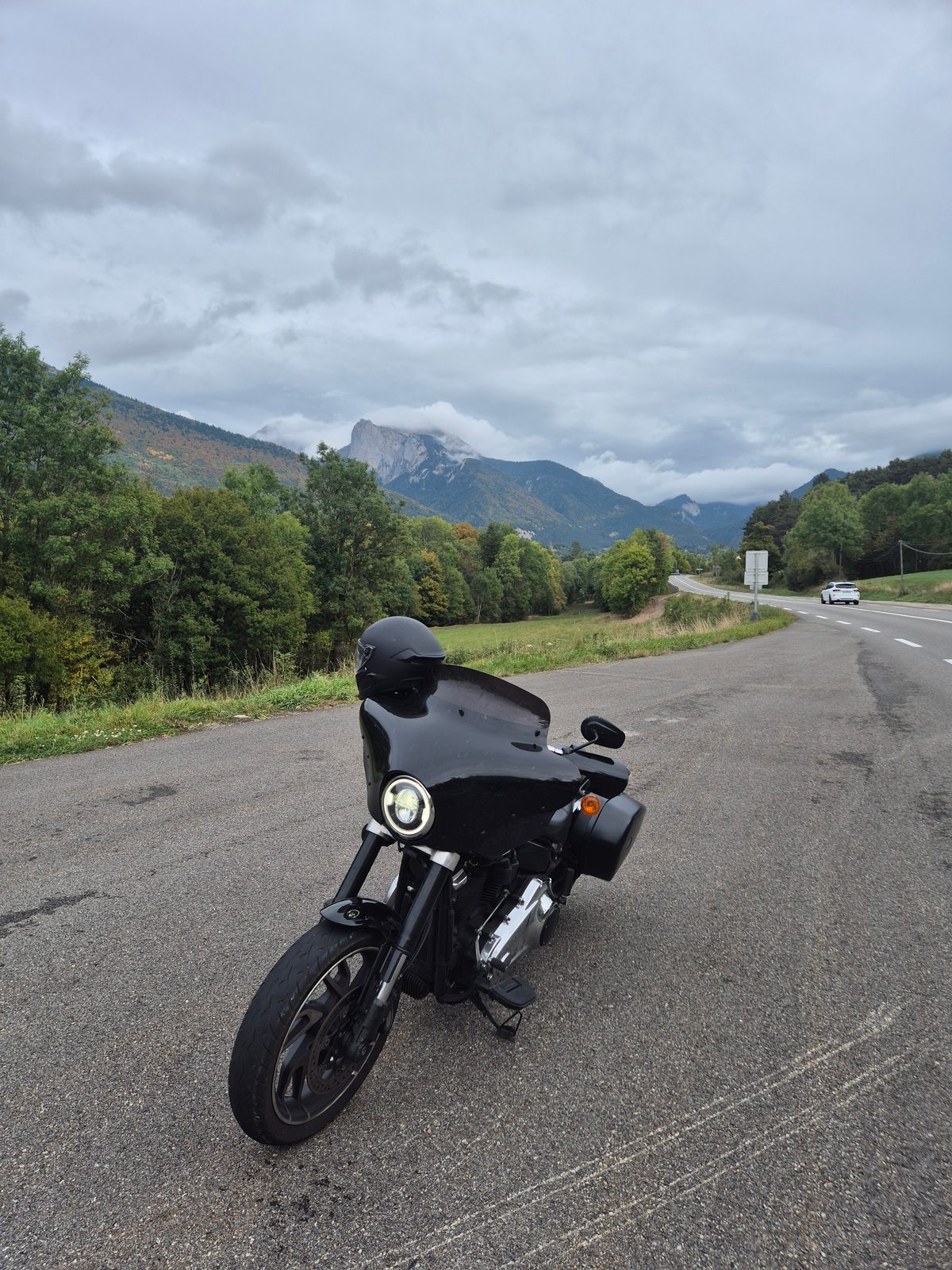 A black Harley-Davidson with a fairing parked at the roadside with cloudy mountains in the background.