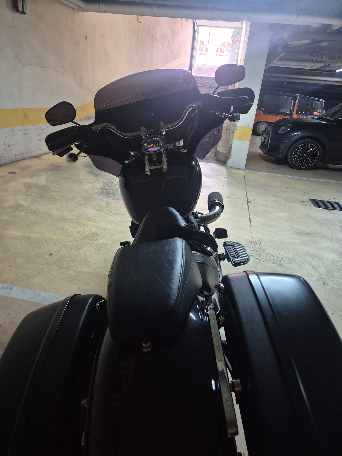 View from behind the seat of a black Harley-Davidson bagger with a fairing and panniers, parked in an underground car park.
