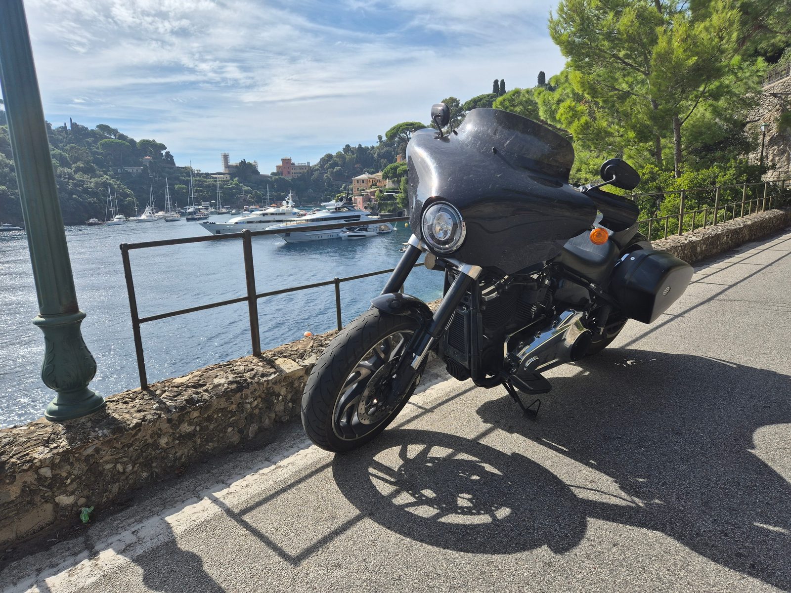 A black Harley-Davidson with a fairing parked beside a railing overlooking a harbour full of yachts and boats.