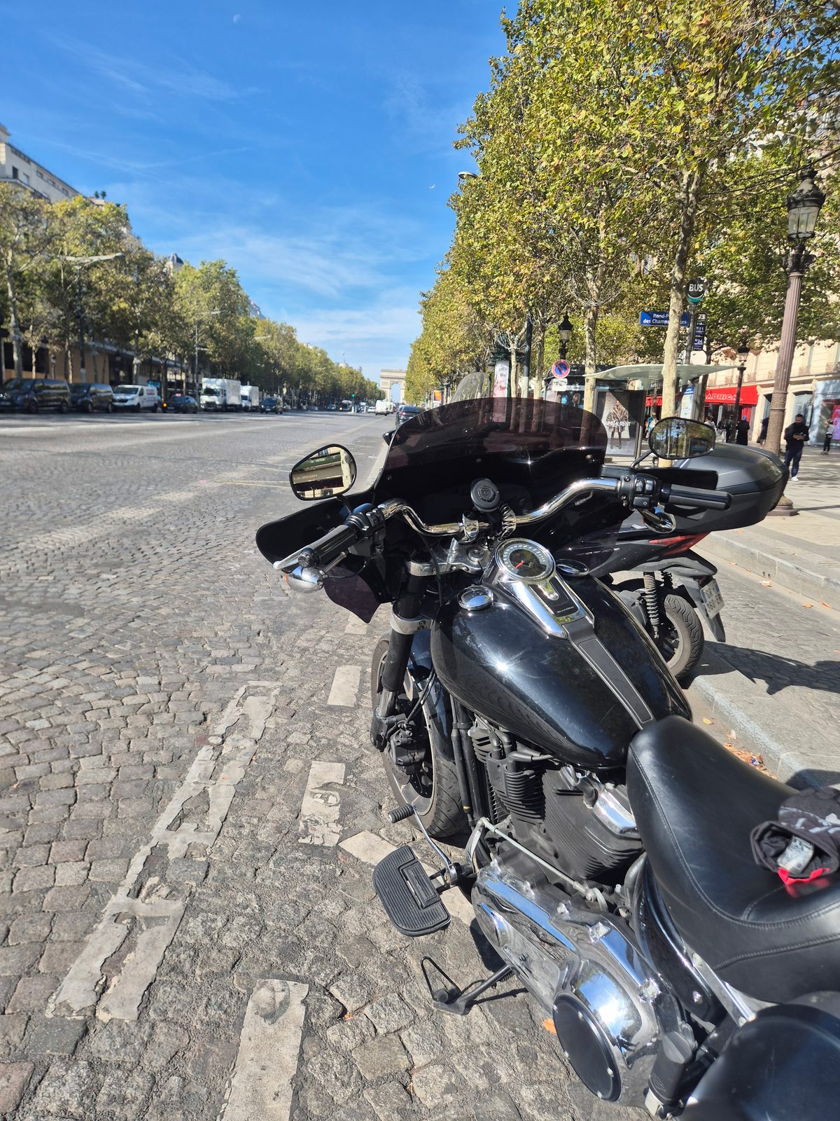 A black Harley-Davidson parked on a cobbled Paris street with the Arc de Triomphe in the distance.