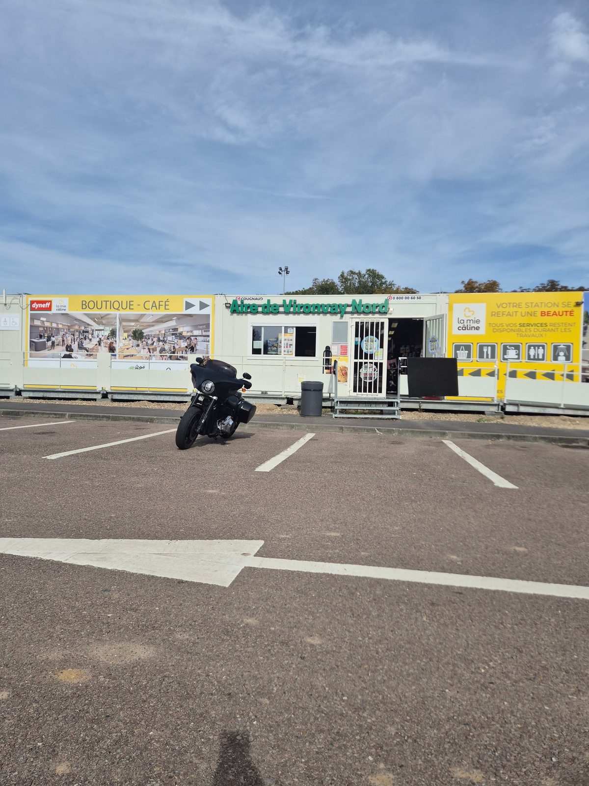 A black touring motorcycle parked in an empty car park outside a motorway service station in France.