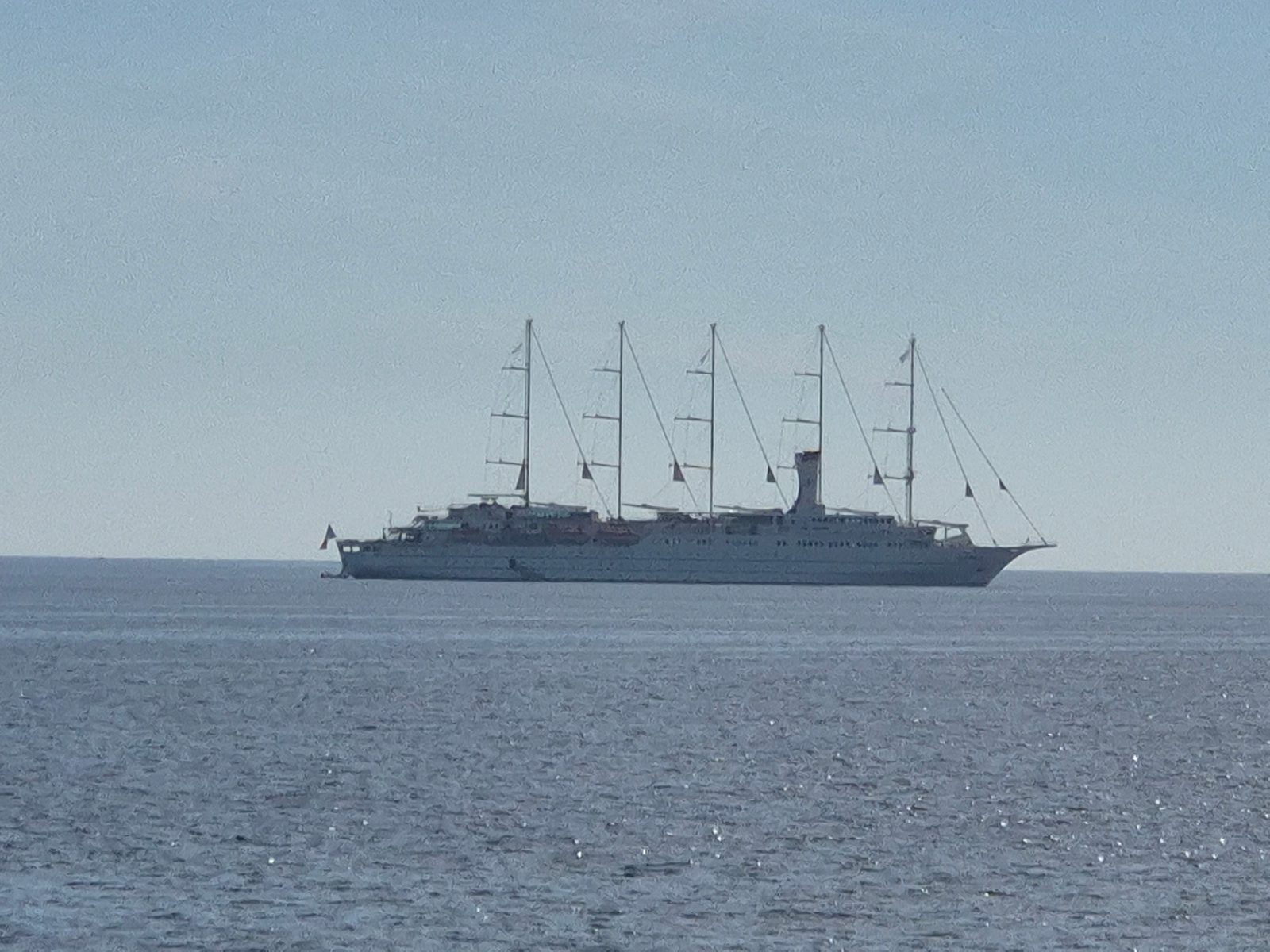 A large five-masted white sailing cruise ship anchored out at sea under a clear sky.