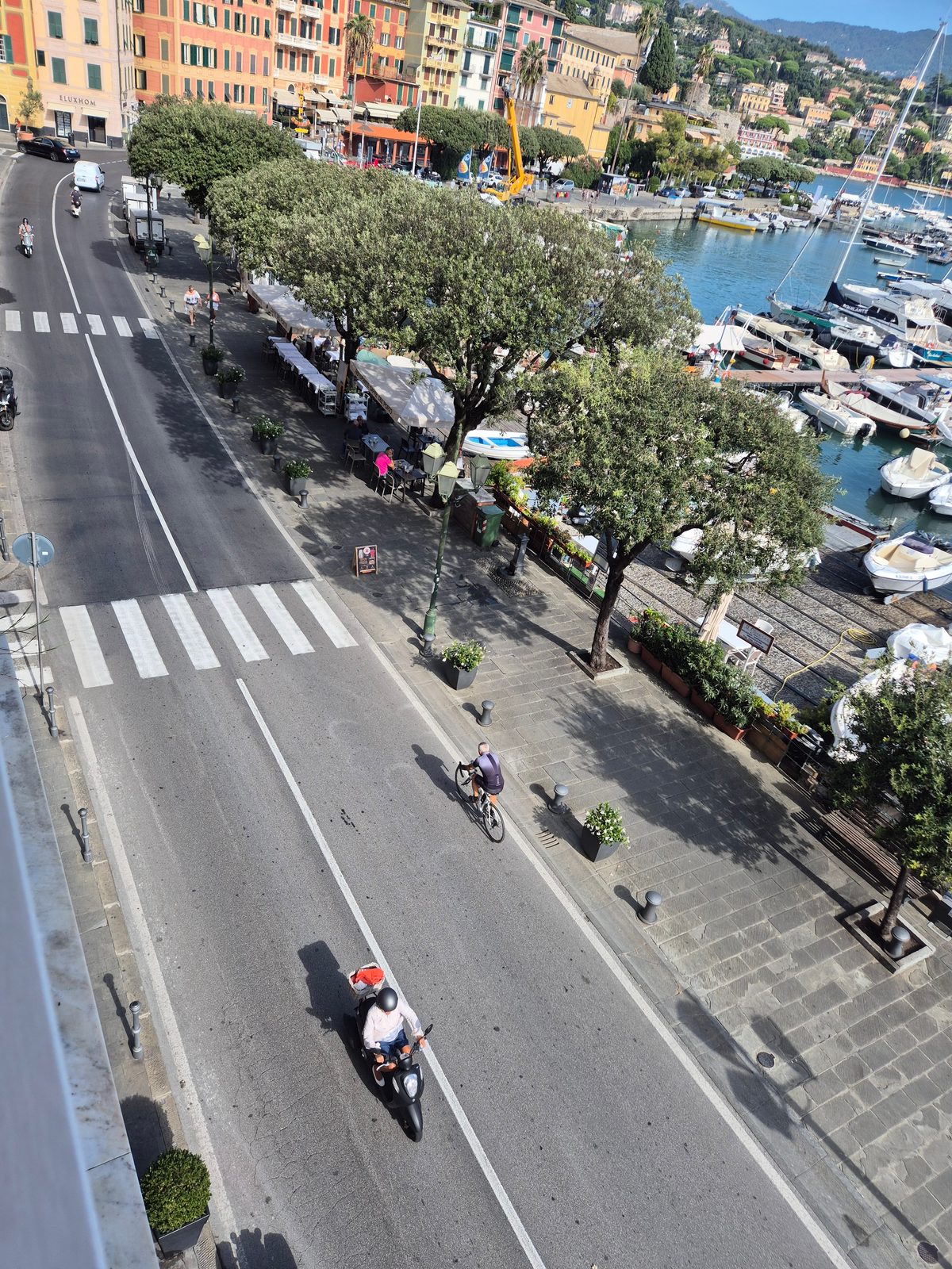 View from above of a seafront road and harbour full of boats, with colourful buildings and hills behind.