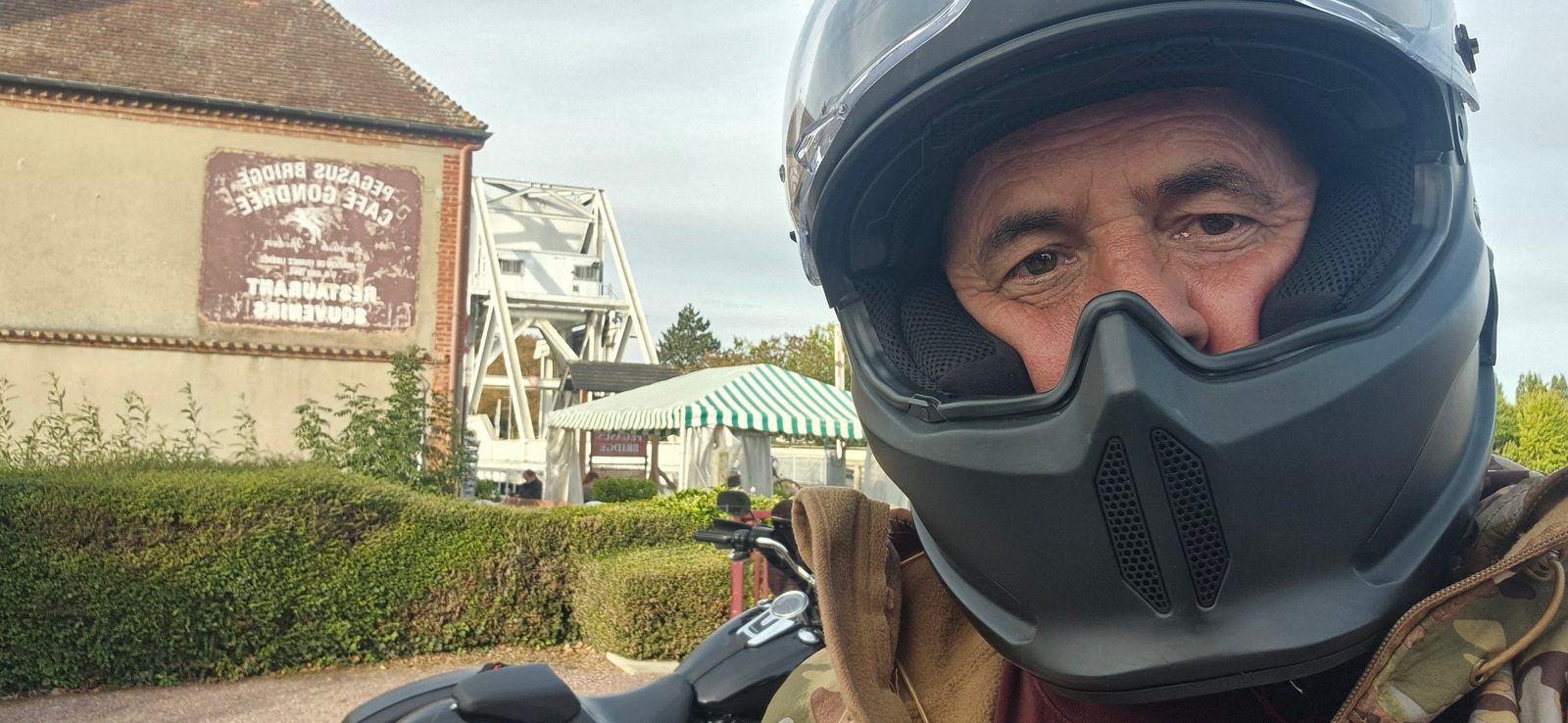 A man in a motorcycle helmet by Pegasus Bridge and the Café Gondrée in Normandy, France.