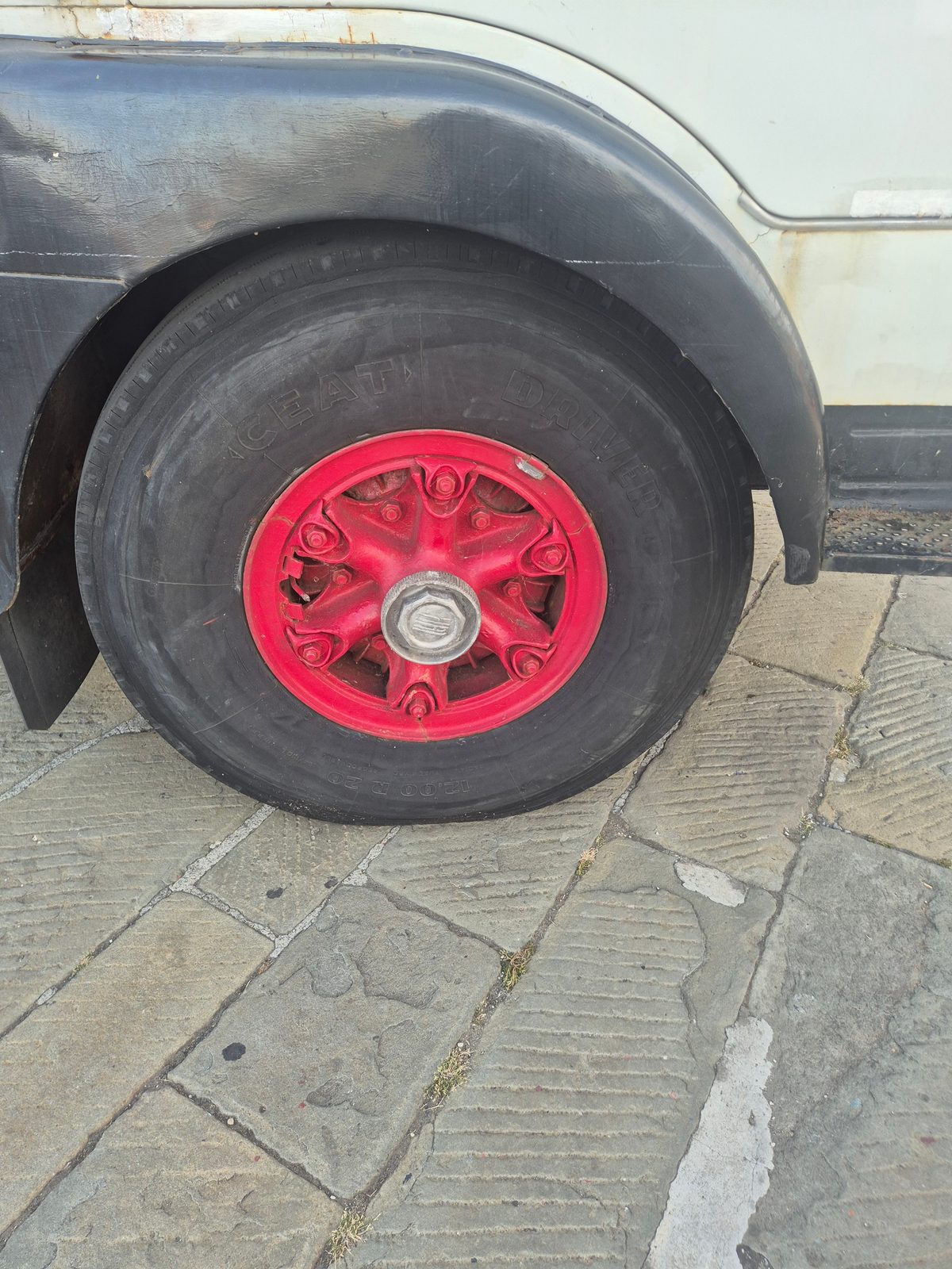 A close-up of an old lorry's wheel with a bright red hub and CEAT tyre, parked on paving stones.