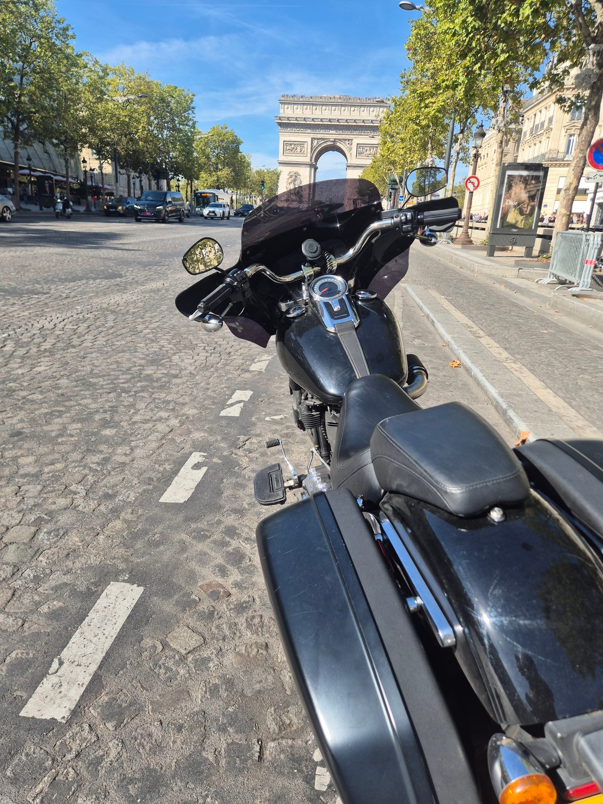A black motorcycle parked on a cobbled Paris street with the Arc de Triomphe in the distance.