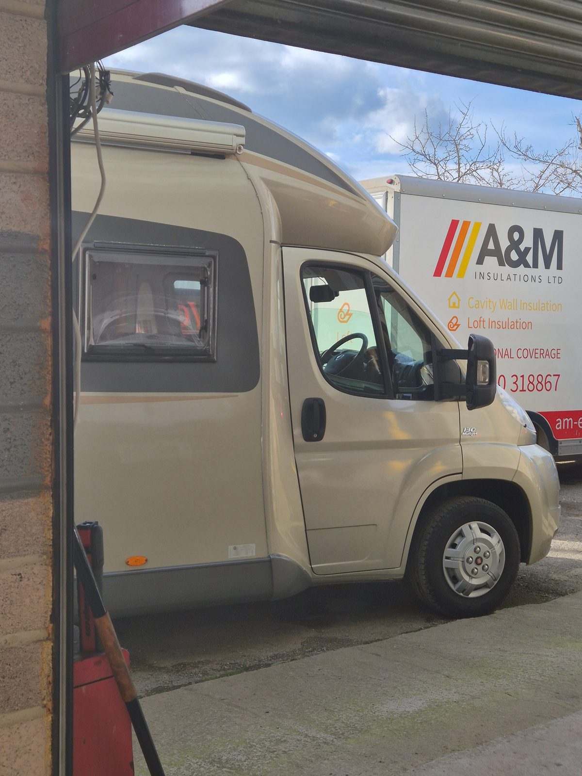 A cream Fiat Ducato 130 Multijet coachbuilt motorhome beside a garage doorway, with an A&M Insulations box van parked behind.