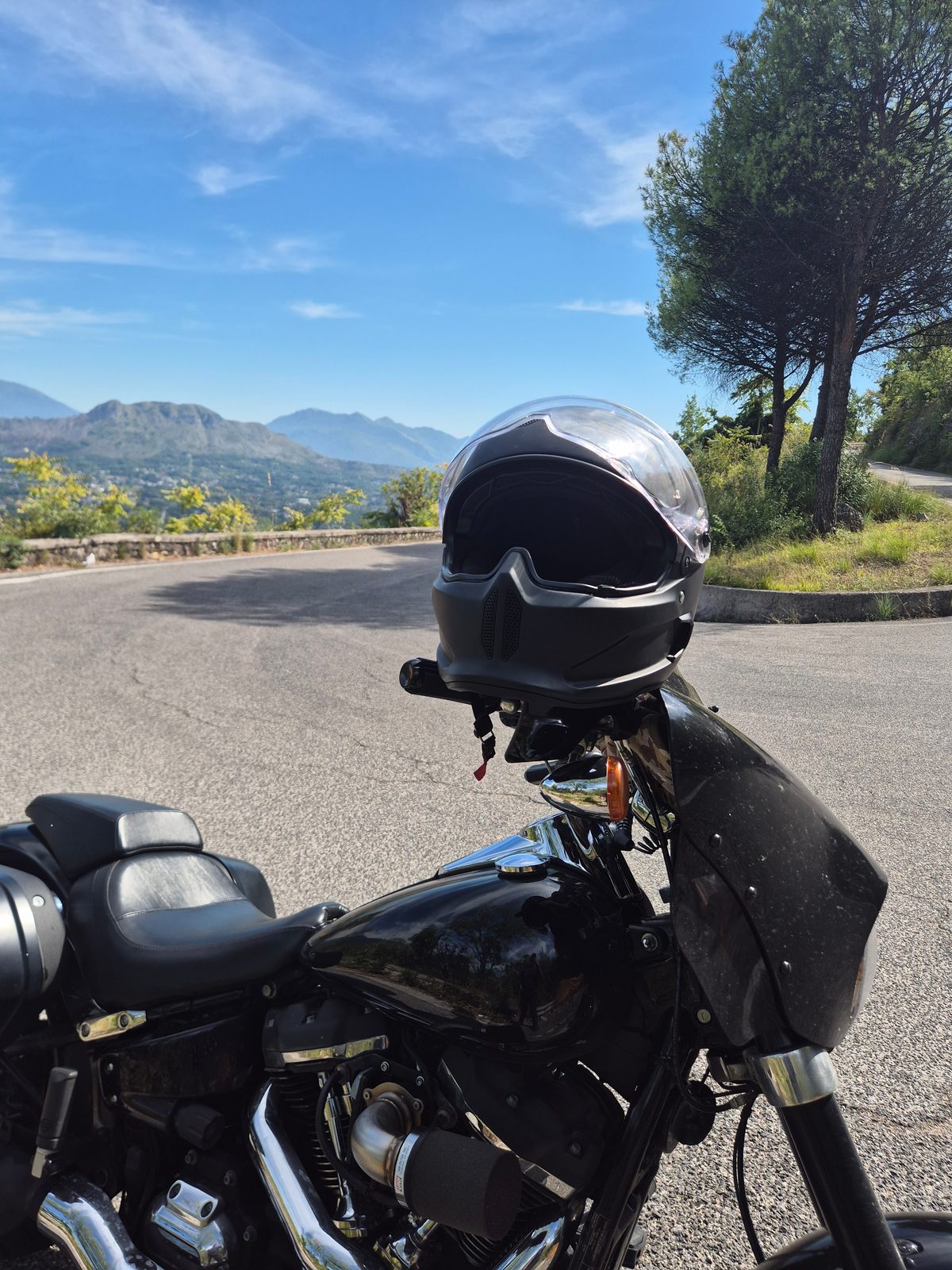 A black Harley-Davidson parked on a mountain road with a helmet resting on the handlebars and hills in the distance.