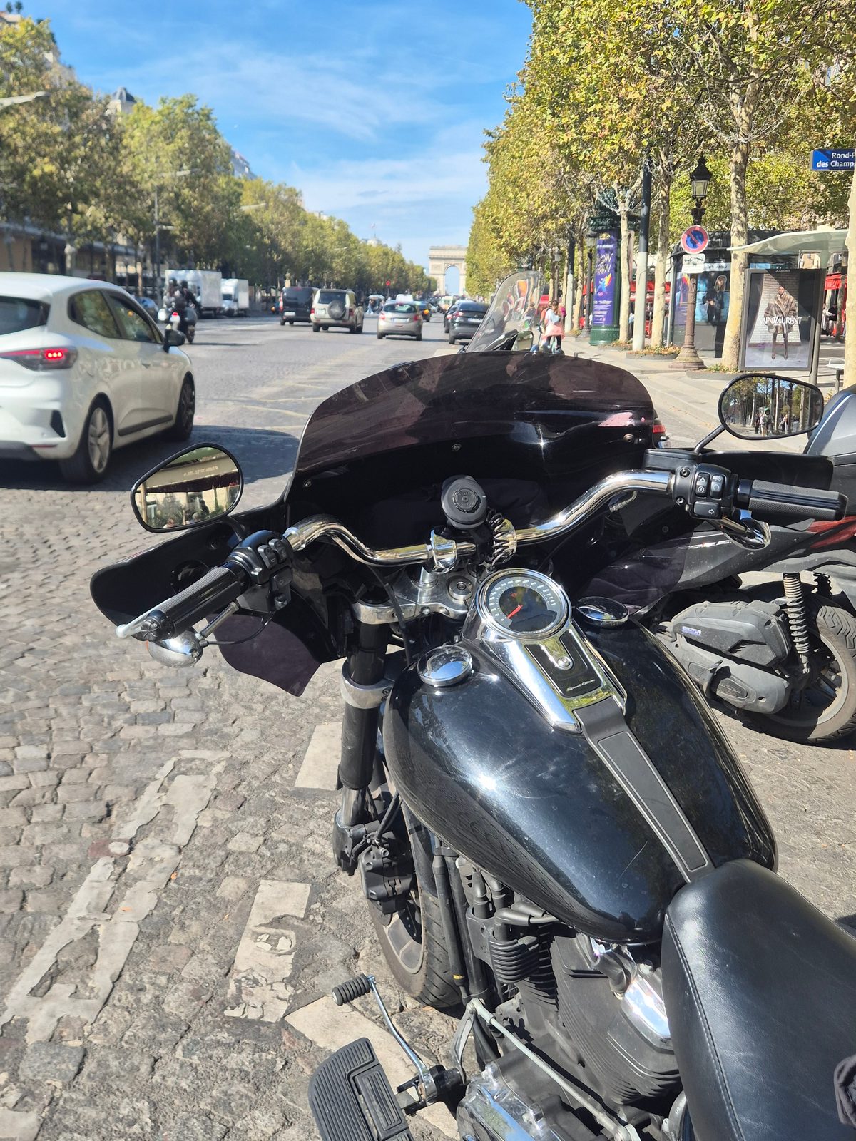 A black motorcycle parked on a cobbled Paris street with the Arc de Triomphe in the distance.