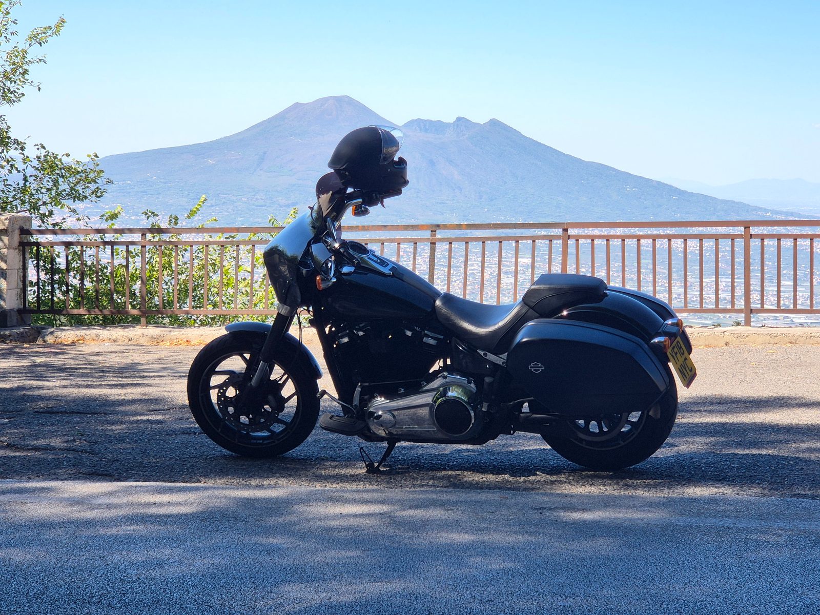 A black Harley-Davidson motorcycle parked by a railing with Mount Vesuvius in the background.