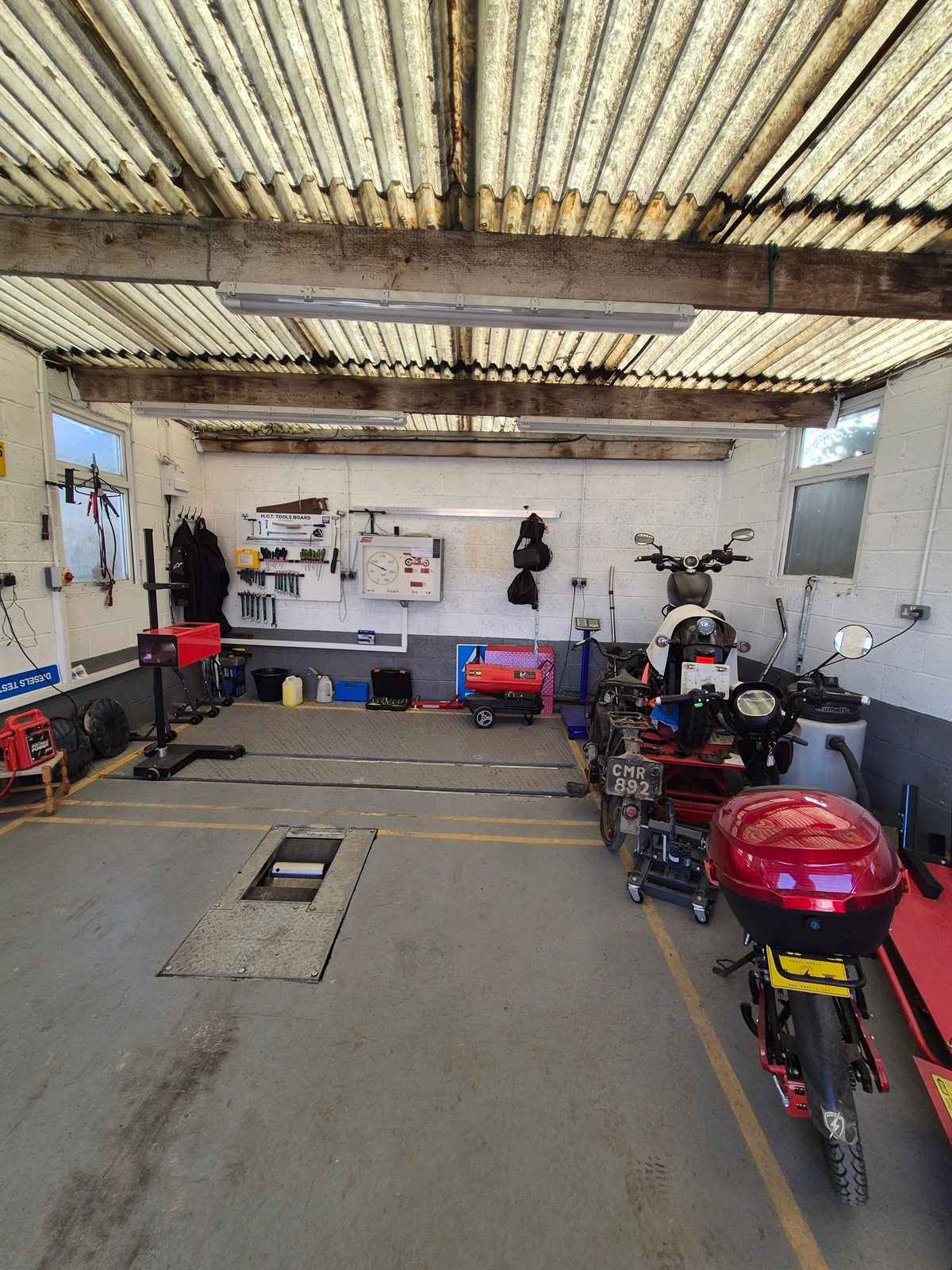 Interior of a motorcycle MOT testing bay with two bikes parked beside a wall of tools and test equipment.