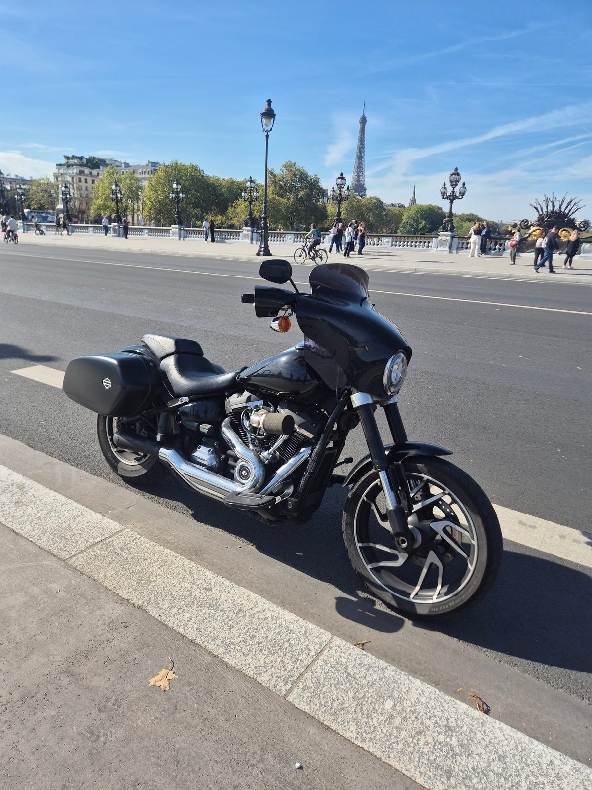 A black Harley-Davidson motorcycle parked on a Paris bridge with the Eiffel Tower in the distance.
