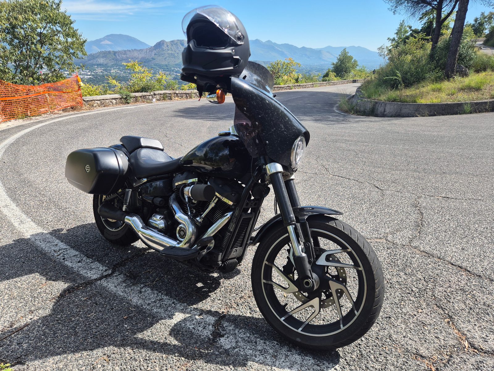 A black Harley-Davidson with panniers and fairing parked on a winding mountain road with hills in the distance.