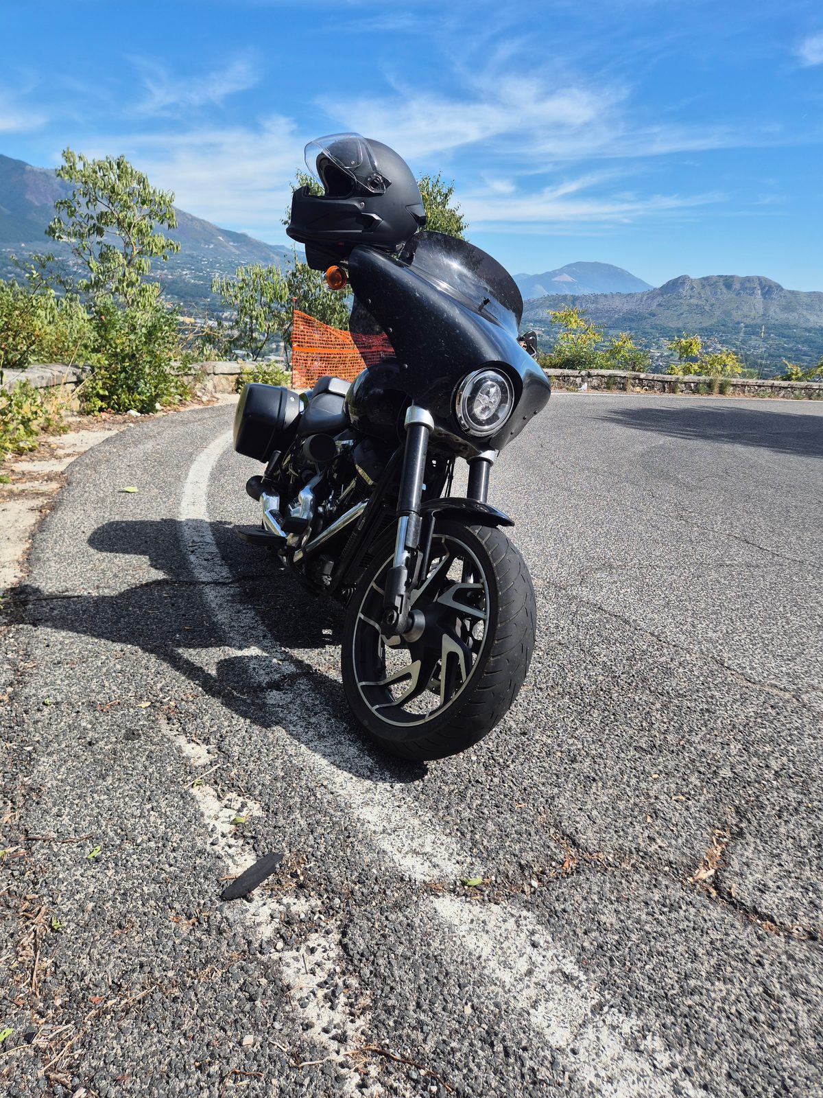 A black Harley-Davidson touring motorcycle parked on a mountain road with hills and valleys in the background.