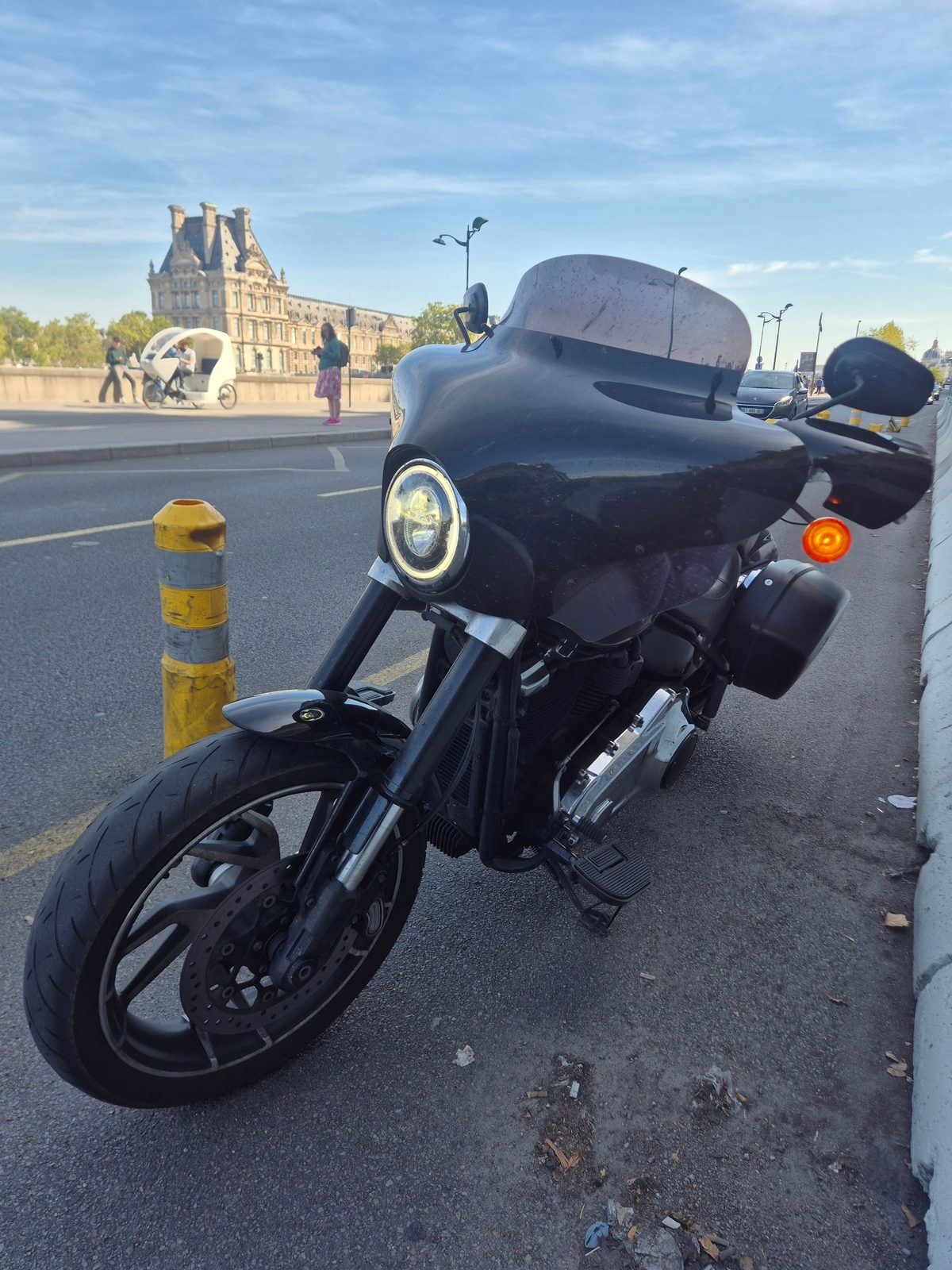 A black Harley-Davidson motorcycle parked at the roadside in Paris with the Louvre in the background.