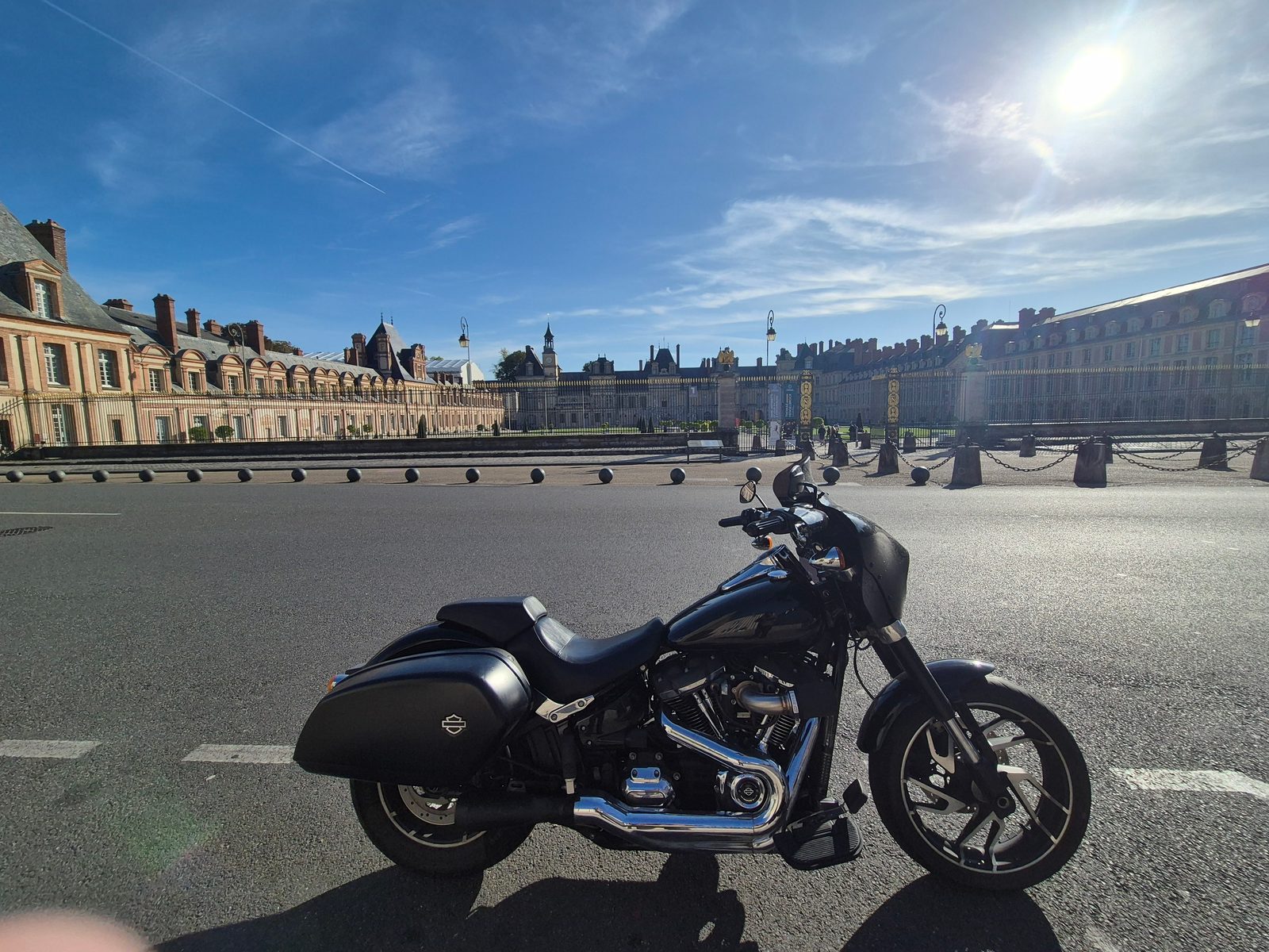 A black Harley-Davidson motorcycle parked on the road in front of the Palace of Fontainebleau under a blue sky.