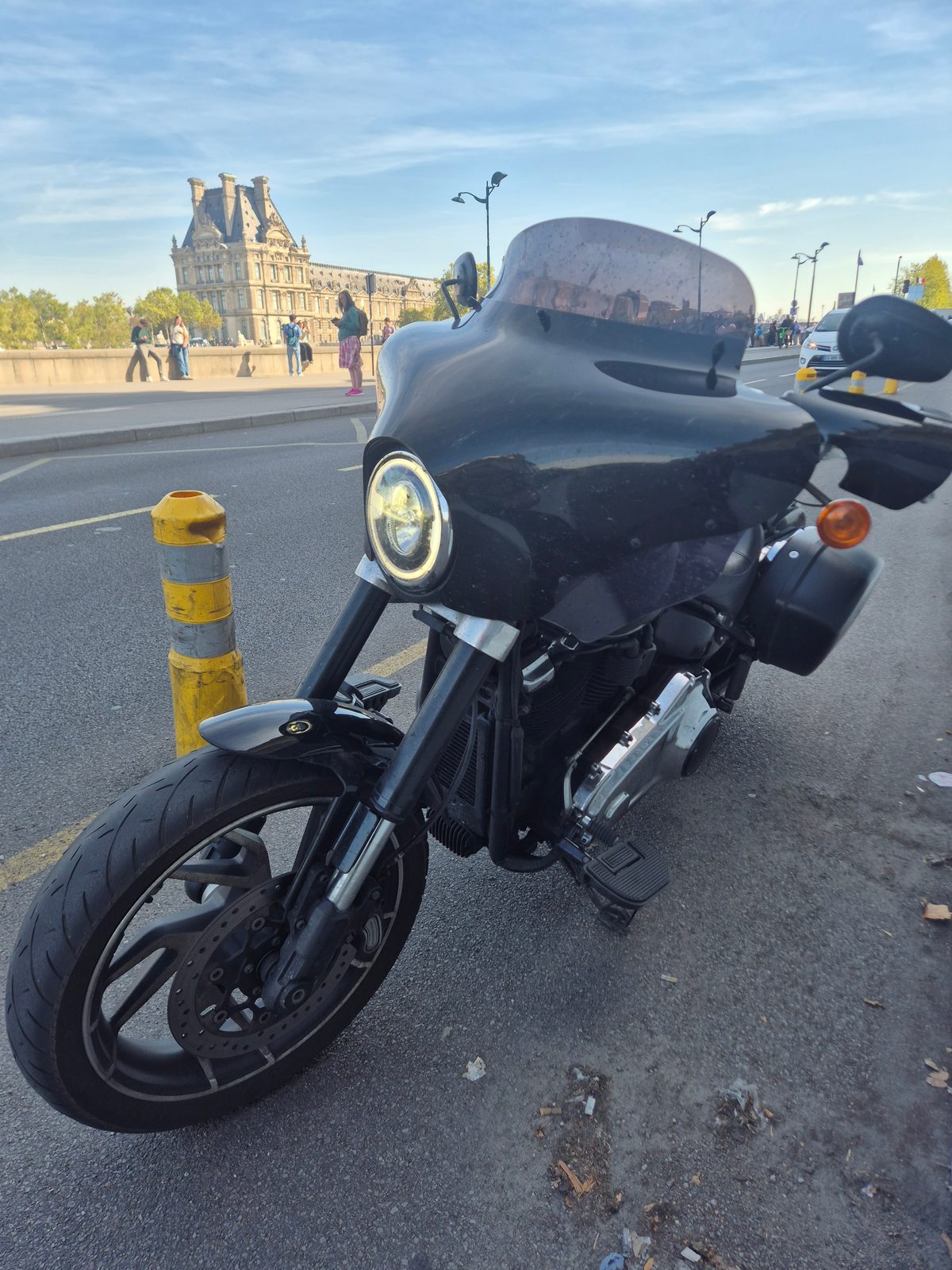 A black Harley-Davidson motorcycle parked on a Paris road with the Louvre in the background.