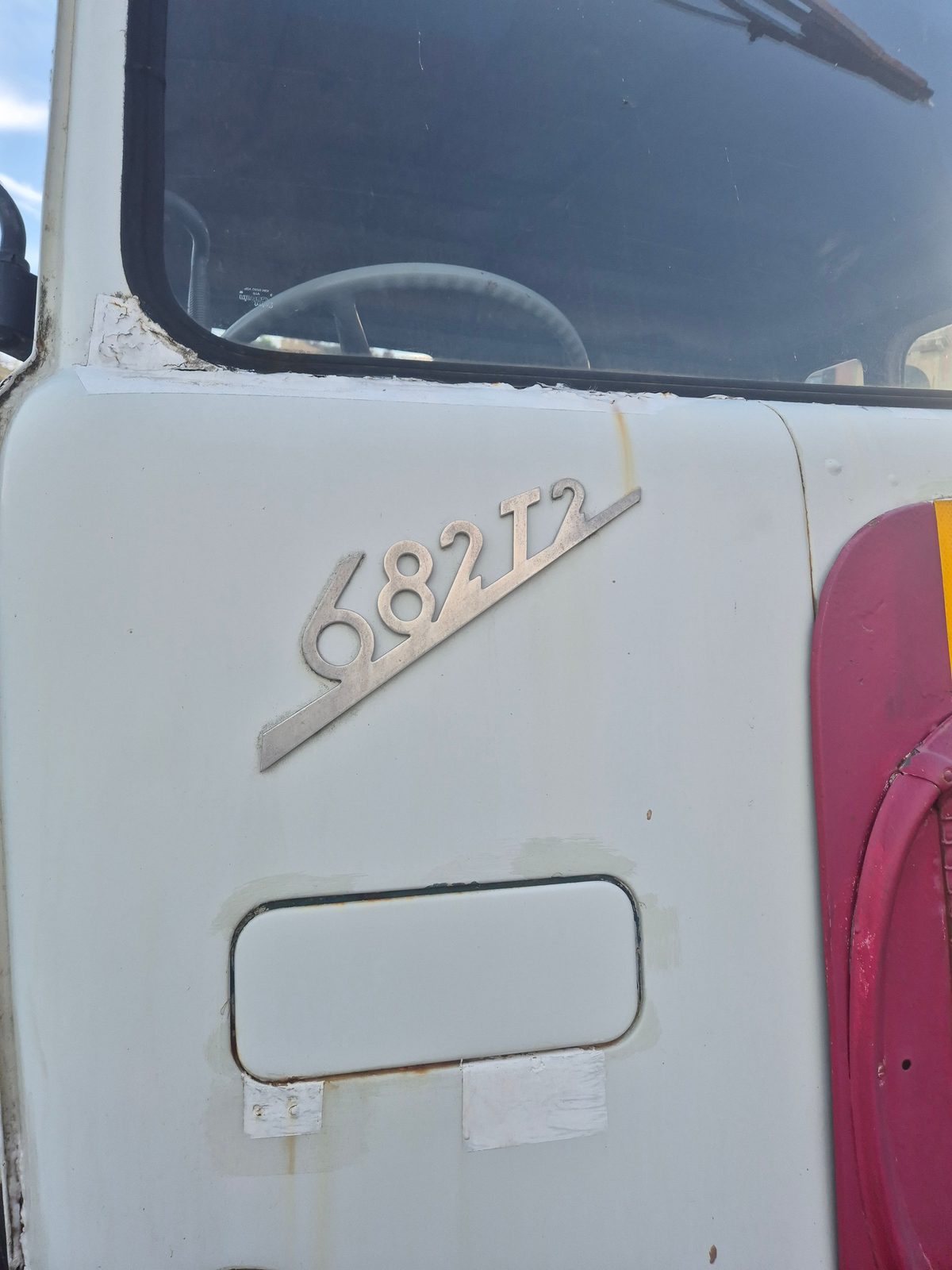Close-up of a white truck cab door with a chrome 682 T2 badge and a red fuel tank beside it.