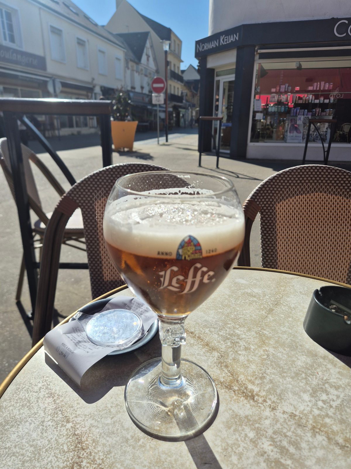 A glass of Leffe beer on a cafe table outside, with a quiet French town street in the background.