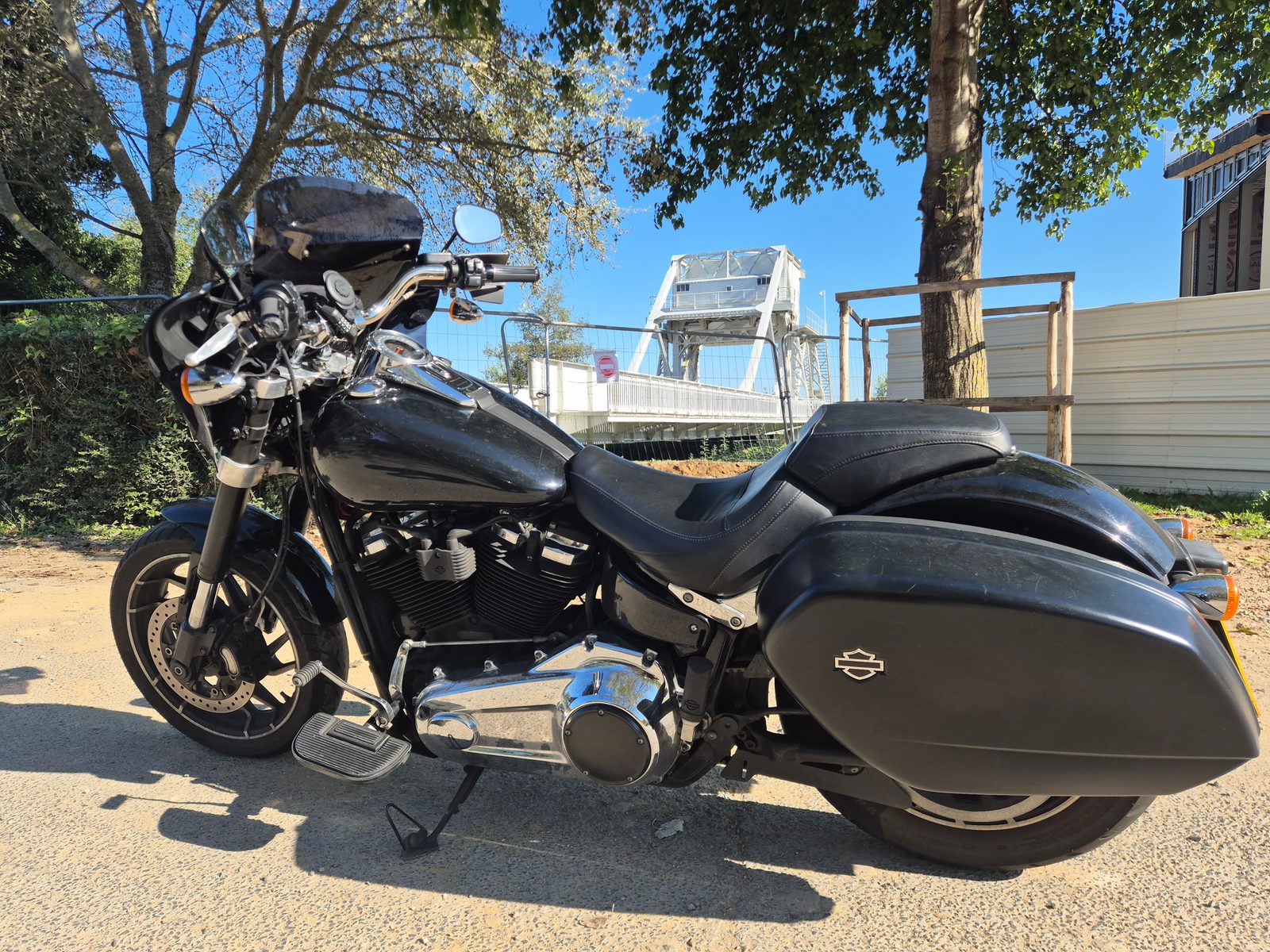 A black Harley-Davidson with panniers parked on gravel in front of Pegasus Bridge in Normandy.
