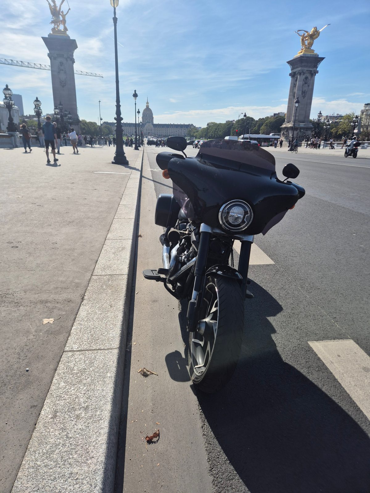 A black Harley-Davidson parked on Pont Alexandre III in Paris with the gilded columns and Les Invalides dome in the background.