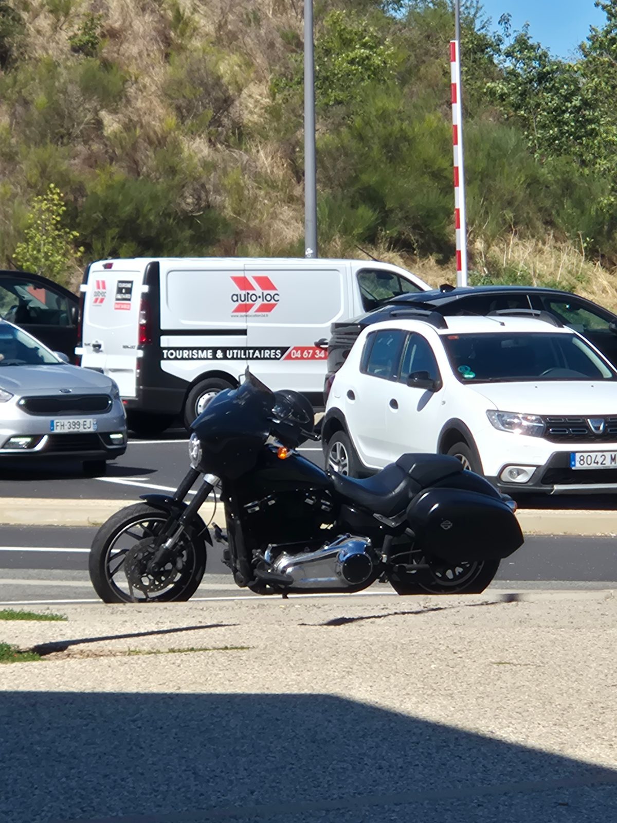 A black Harley-Davidson motorcycle with panniers parked in a car park next to a white van and cars.