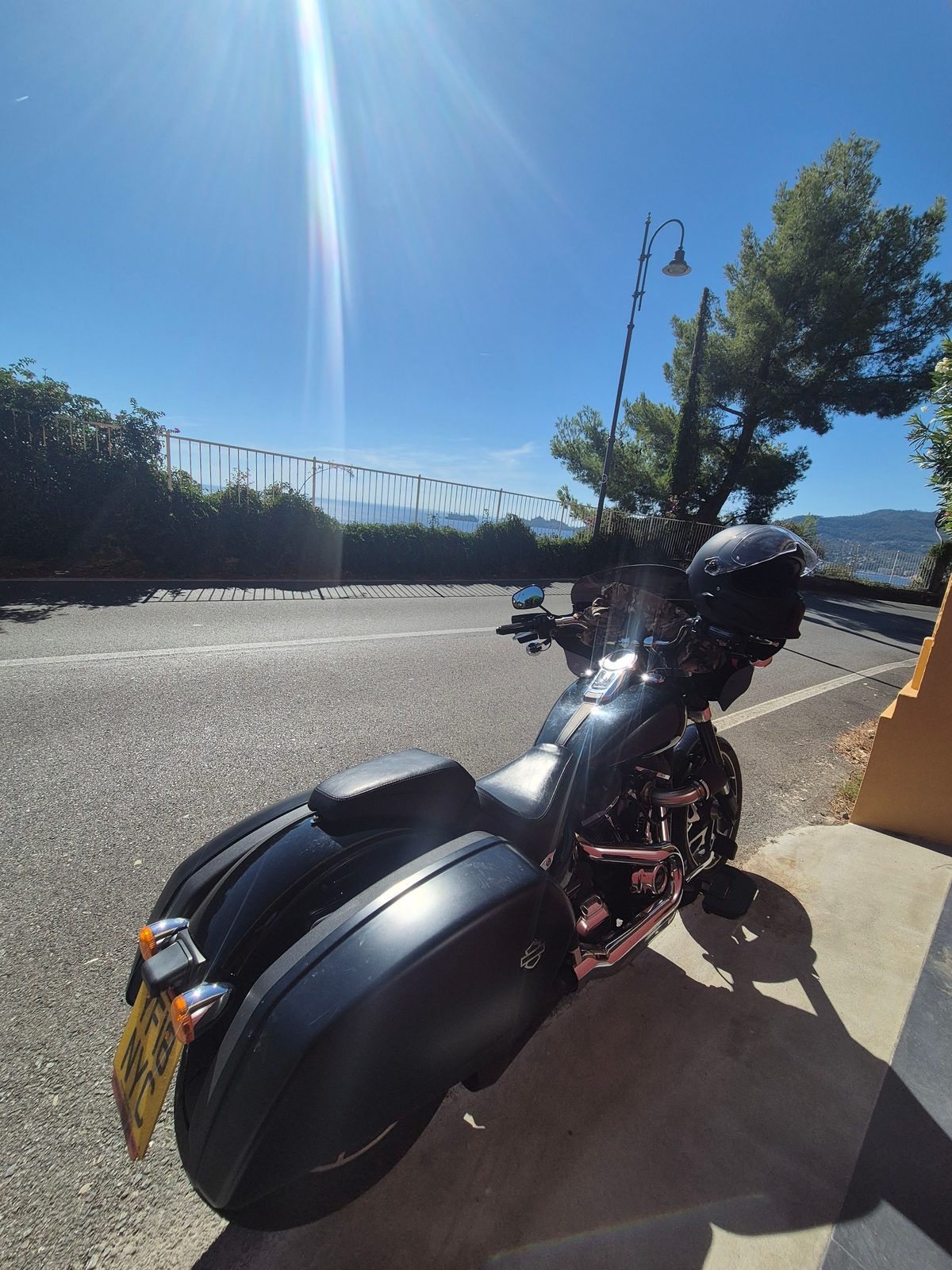 A black Harley-Davidson with panniers and a helmet resting on it, parked by a roadside overlooking the sea.